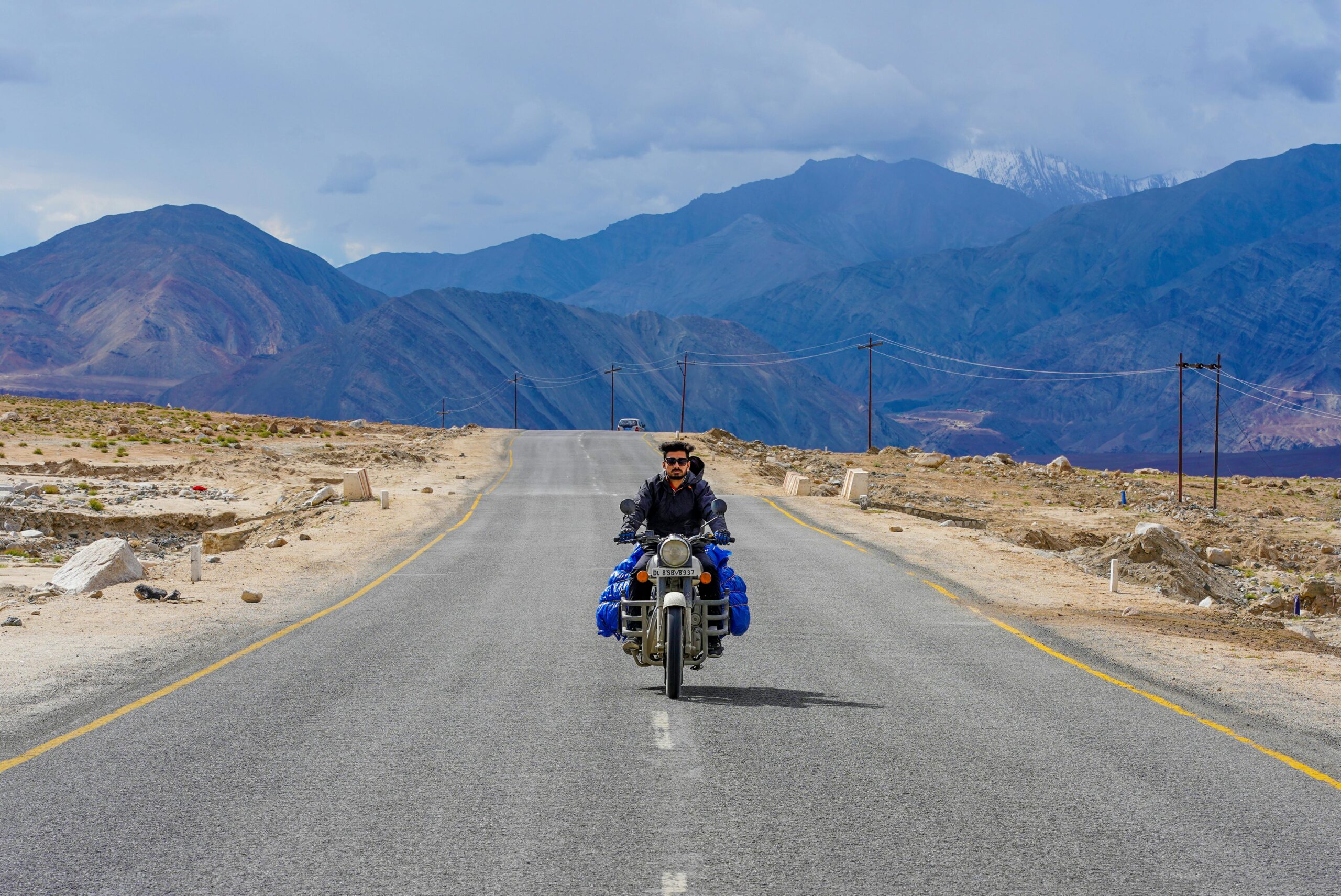 A solitary biker traveling through the rugged terrain of Leh, surrounded by majestic mountains.